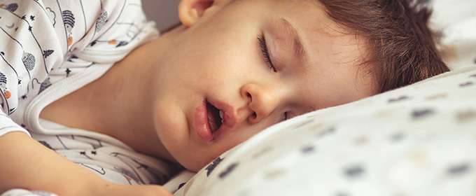 a young boy wearing patterned pajamas sleeping on a polka-dot bed